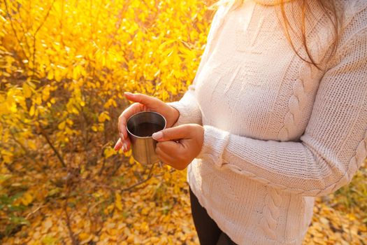 Girl holding a hot drink on a background of autumn foliage. High quality photo