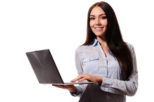 Beautiful young business woman with long hair in a denim shirt, keeps laptop in hand, smiling, looking at camera, on a white background