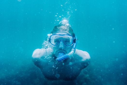 Freediver young man in mask and snorkel swimming underwater in blue sea.