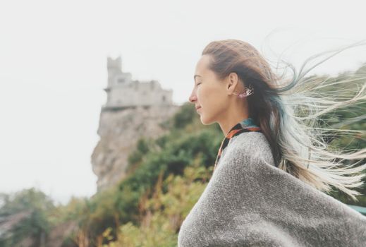 Smiling young woman standing in windy weather on background of Swallow's Nest, Crimea, Russia.