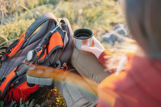 Explorer young woman rests with cup of tea and backpack in summer.