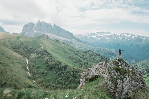 Hiker standing on peak of cliff with raised arms on background of summer mountains. Small figure of explorer on nature.