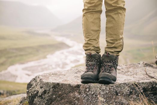 Hiker woman standing on rocky stone on background of mountain river, view of legs.