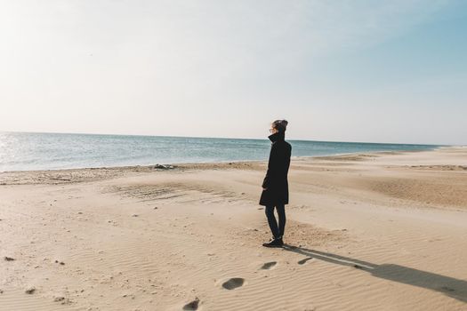 Young woman walking on sandy shore and enjoying view of sea in autumn.