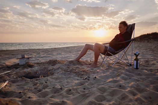 Young man resting on sand beach near the sea at sunset.