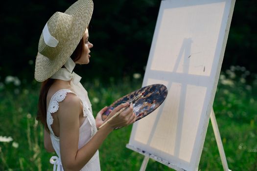 Woman in white dress paints a picture on nature easel. High quality photo