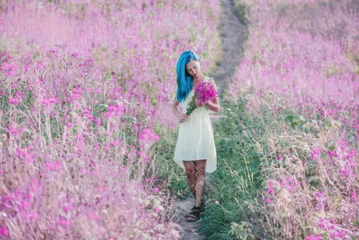Beautiful young woman with blue hair picking purple flowers on summer meadow.