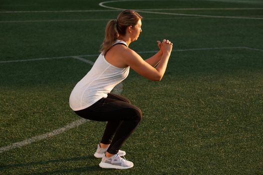 Sports girl squatting on the stadium lawn. High quality photo
