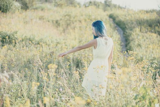 Beautiful young woman walking on yellow wildflower meadow in summer.