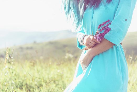 Unrecognizable young woman walking with flowers on summer meadow, view of hands.