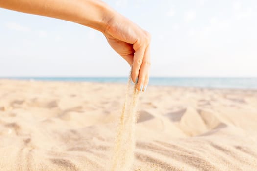 Female hand pours sand on beach near the sea.