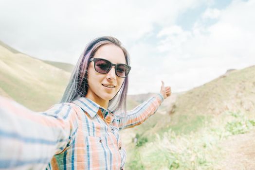 Happy young woman taking self-portrait in summer mountains, point of view.
