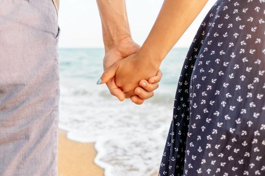 Couple in love holding hands on sand beach, close-up.