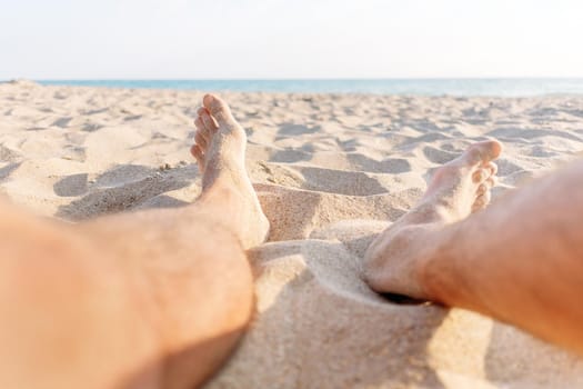 Young man sitting on sand beach, view of legs, pov image.