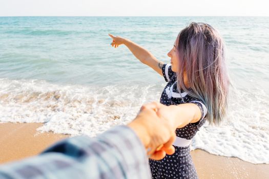 Couple in love. Beautiful young woman holding man's hand and pointing at sea. Point of view shot.