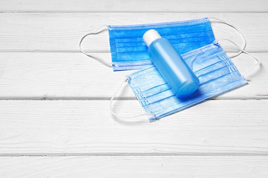 Medical face mask and sanitizer gel on white wooden background close up
