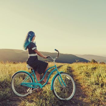 Young woman wearing in dress sitting on cruiser bicycle and enjoying view of nature.
