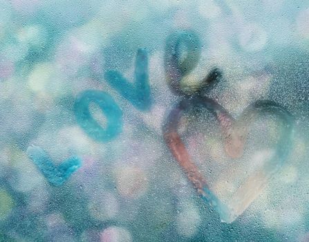Heart shape and word love written on glass with water drops in rainy weather in front of defocused city lights.