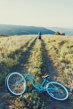 Young woman walking on summer meadow, in the foreground a bicycle cruiser.