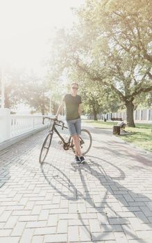 Handsome young man standing with bicycle in summer park.