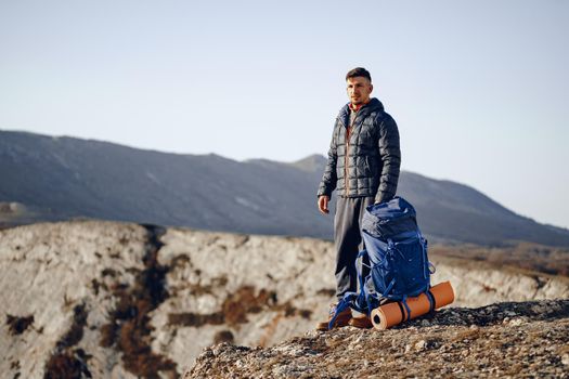 Male backpacker or hiker in hiking equipment standing at the top of the mountain