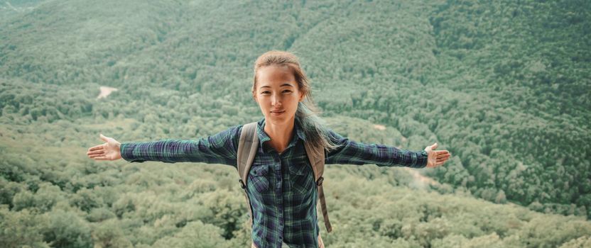 Explorer young woman standing with raised arms on background of summer valley, front view.