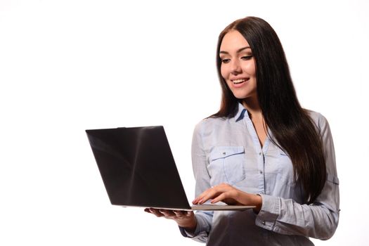 Happy attractive young woman in denim shirt standing and looks screen laptop over white background