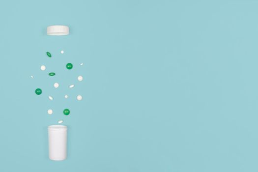Medical background with pills. White and green pills pour out of a bottle on a blue background. Flat lay concept. Copy space.