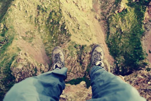 Hiker man sitting on edge of cliff in the mountains, view of legs, pov image.