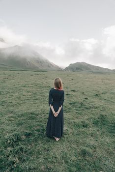 Young woman wearing in long dress walking in summer mountains, rear view.