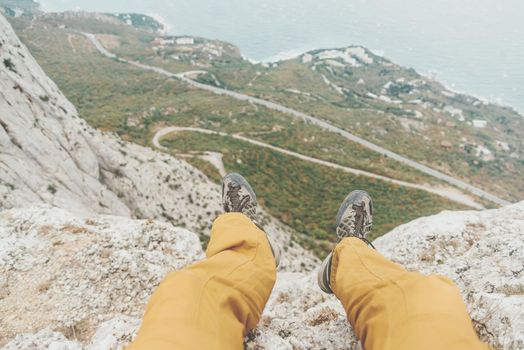 Man sitting on edge of cliff over coastline, view of legs, pov.
