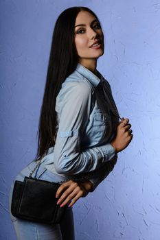 fashion girl, beautiful young woman posing at studio in jeans with bag