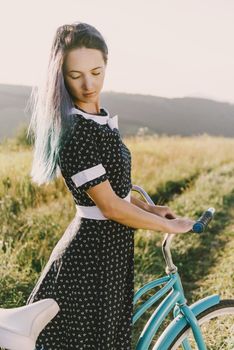 Beautiful young woman in dress standing with bicycle cruiser outdoor.