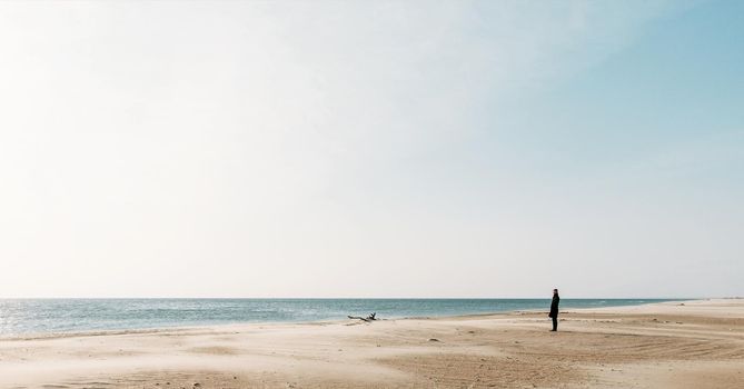 Lonely young woman walking on sandy coastline and enjoying view of sea.