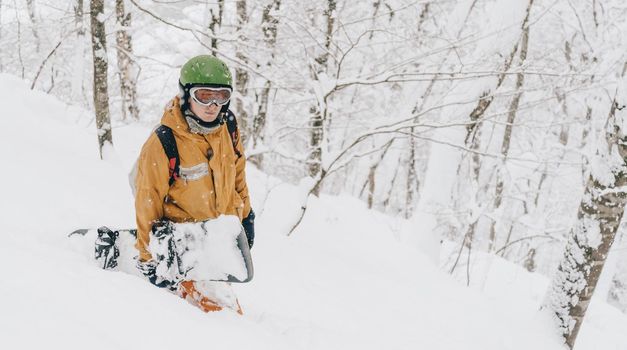 Sporty young man wearing in protective clothing walking with snowboard in winter forest after a snowfall.