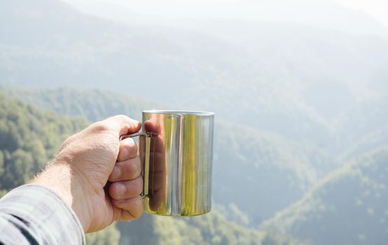 Traveler man drinking tea in the mountains. View of male hand with cup outdoor. Point of view shot.