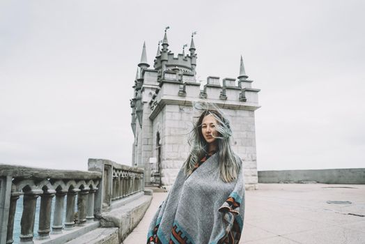 Young woman standing on background of castle Swallow's Nest in windy weather, Crimea, Russia