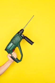 Green Puncher in the hands of a builder. Female hand hold new Puncher or drill isolated on yellow background