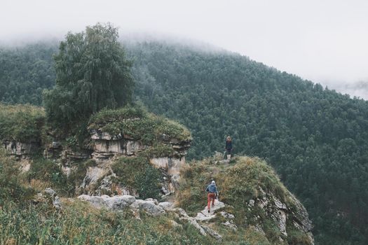 Couple walking on a high cliff covered with greenery among summer mountains.