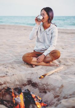 Young woman resting on sand beach near a campfire on background of sea.