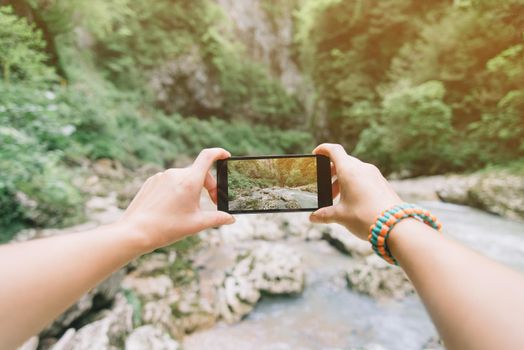 Traveler woman taking a photo with smartphone river in summer, point of view.