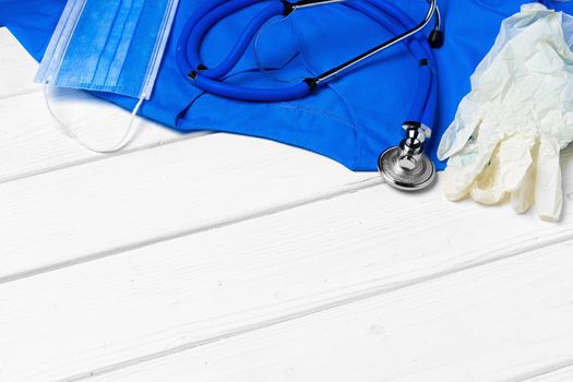 Doctor medical uniform with stethoscope and face mask on white wooden background close up