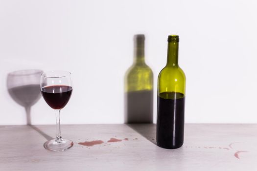 Bottle with wine and glass, red puddle of wine on the table. Cleaning after party concept