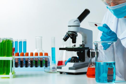 Woman scientist looking at slide with blood sample near microscope in laboratory. Blood test