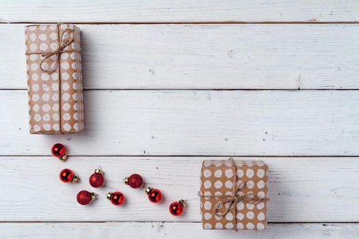 Packed small Christmas gifts and red baubles on white wooden board top view