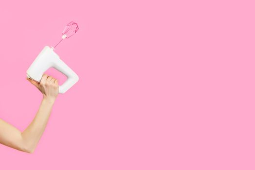 White kitchen mixer in female hand isolated on pink background. Copy space. Modern kitchen or woman power concept