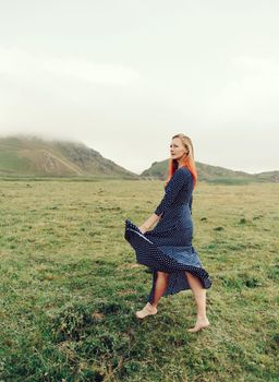 Beautiful barefoot young woman in long dress walking on summer meadow in the mountains.
