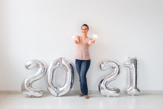New Year celebration and party concept - Happy young woman with sparklers near silver 2021 balloons on white background
