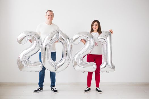 New 2021 Year is coming concept - Happy young man and woman are holding silver colored numbers indoors