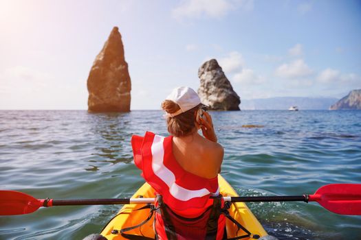 Young brunette woman in red swimsuit and Santa hat, swimming on kayak around basalt rocks like in Iceland. Back view. Christmas and travel concept